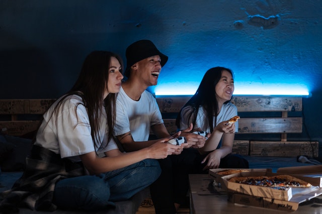 Three friends eating pizza and playing a computer game